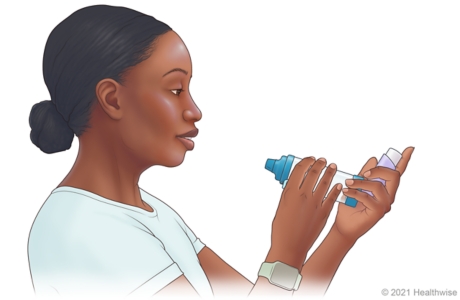 Person holding inhaler and spacer so that inhaler mouthpiece is at bottom. Person holding inhaler and spacer so that inhaler mouthpiece is at bottom.