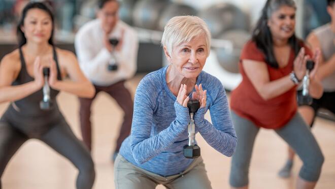Group fitness class with people lifting dumbbells while squatting